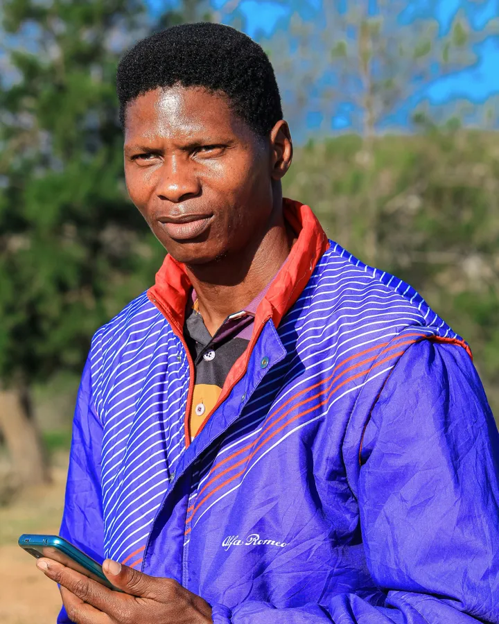 A man in a violet jacket checks his phone outdoors.
